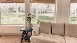 Un salon avec un canapé beige, une petite table sur laquelle est posé un vase, et de grandes fenêtres donnant sur une cour.