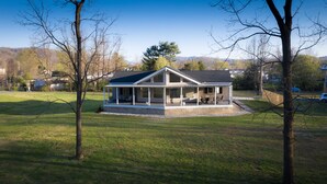 Une maison dotée d’un porche abrité, de fondations en pierre et offrant une vue sur une cour verdoyante et des arbres.