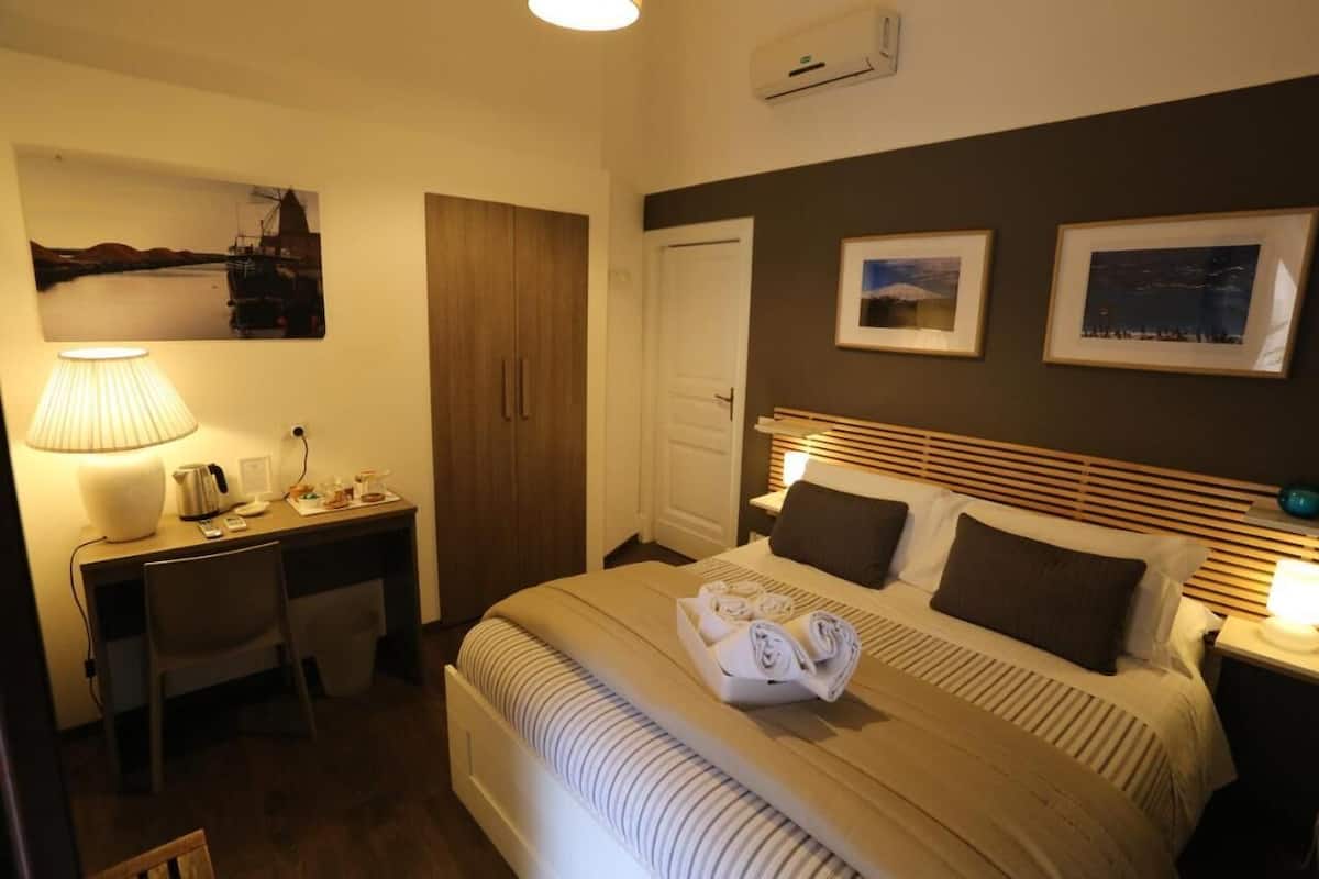 Habitación de hotel con cama, escritorio, silla, lámpara y aire acondicionado instalado en la pared.