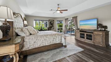 A bedroom with a bed, a television, a ceiling fan, and a view of the outdoors.