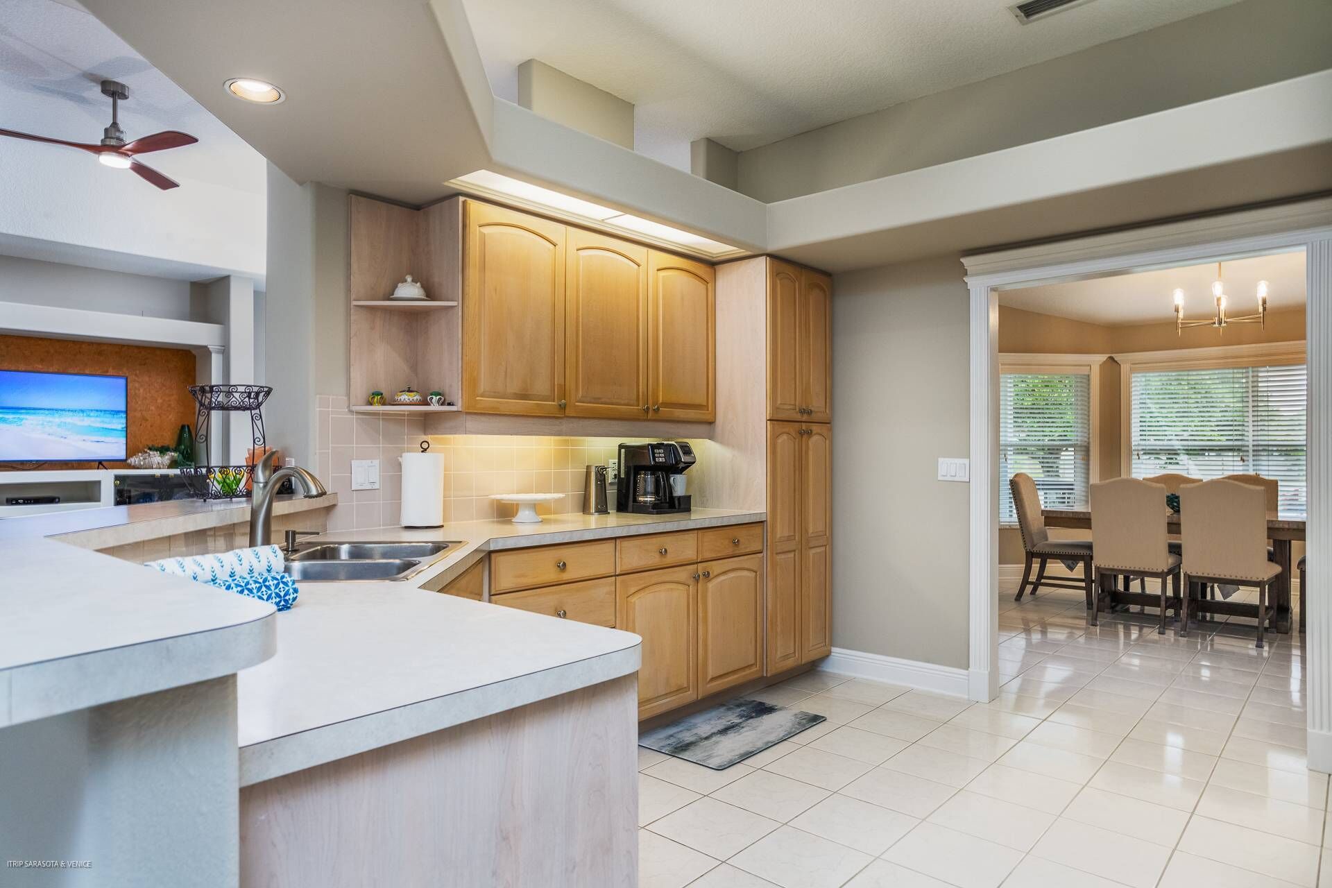 A modern kitchen with wooden cabinets, a built-in oven, a coffee maker, and a dining area with a table and chairs.