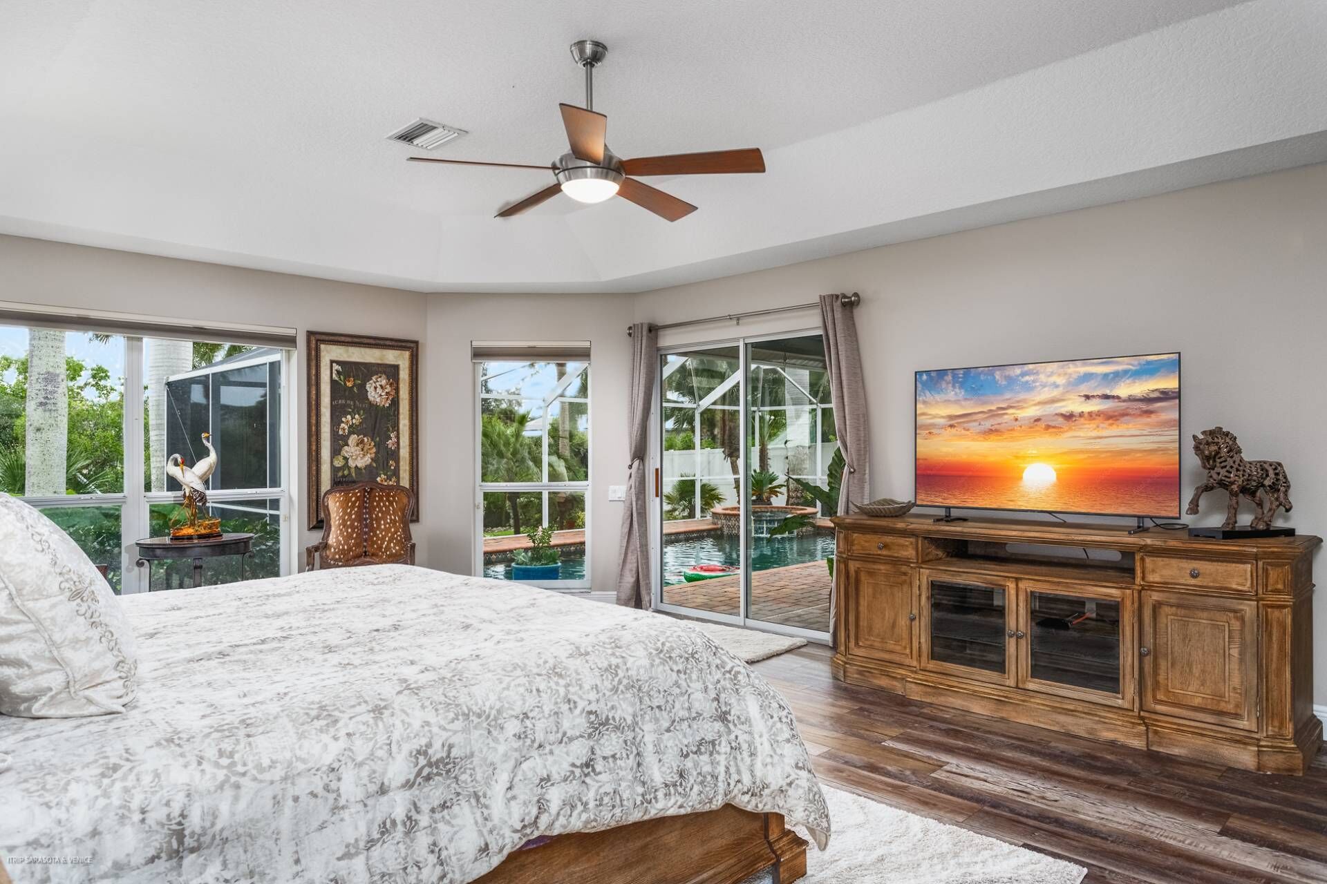 A bedroom with a large bed, a ceiling fan, a TV, and a view of a swimming pool through glass doors.