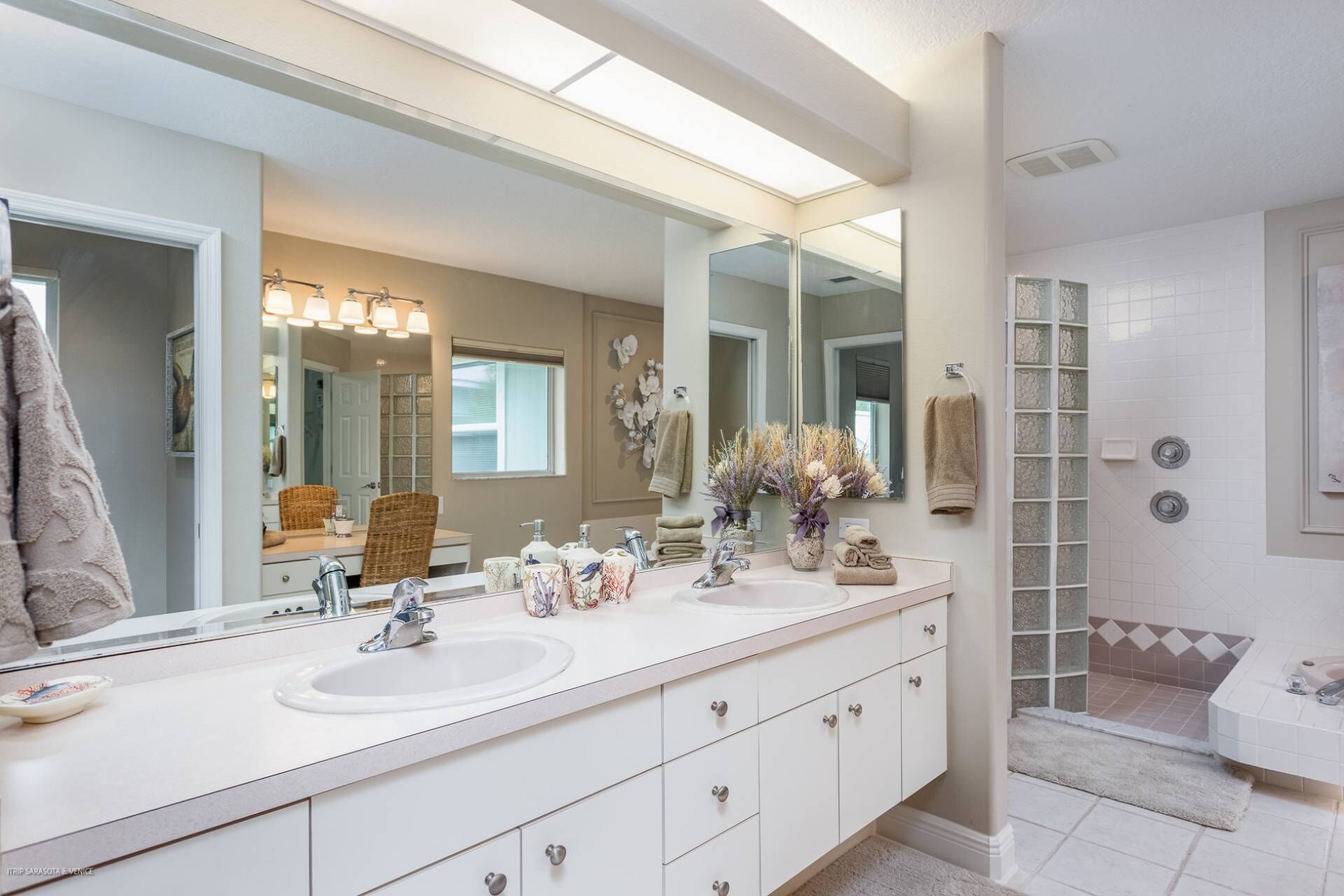 A modern bathroom with two sinks, a large mirror, and a glass shower enclosure.