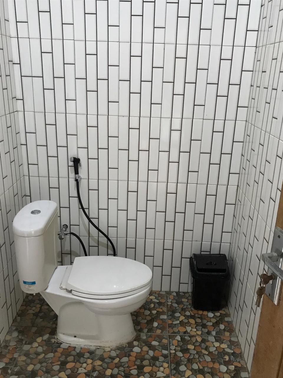 A bathroom with a toilet, a black trash bin, and a tiled wall.