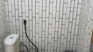 A bathroom with a toilet, a black trash bin, and a tiled wall.