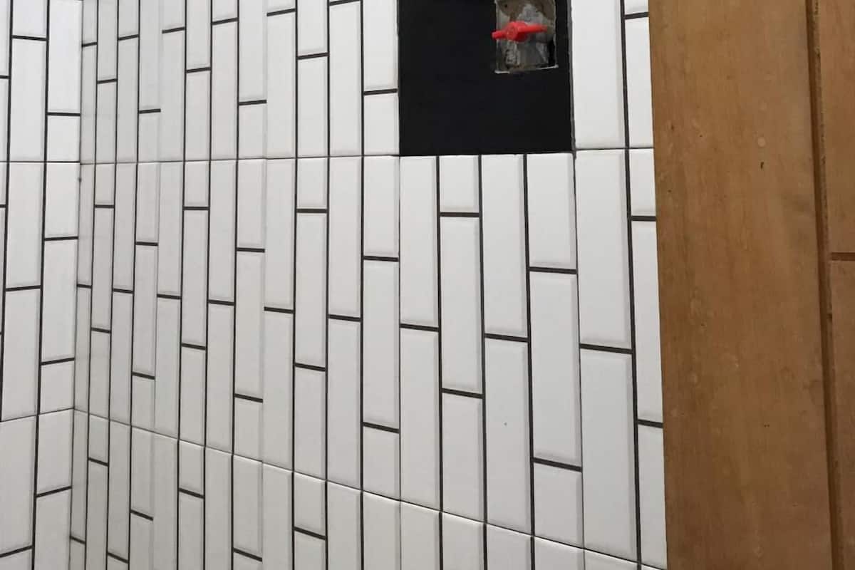 Ein Duschbereich mit weißen und schwarzen Fliesen, einem Duschkopf und einer Holztür.