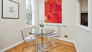 Ein zeitgemäßer Essbereich mit einem Glastisch und Stühlen, einem roten abstrakten Gemälde und einem gerahmten Kunstwerk an der Wand.