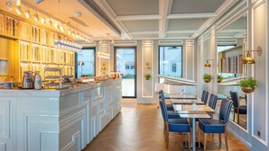 Un restaurant moderne doté d’un bar, de bibliothèques en bois et d’un espace repas avec des chaises bleues et une longue table.
