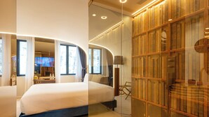 Une chambre d’hôtel moderne avec un grand lit, une cloison en verre et une bibliothèque remplie de livres.