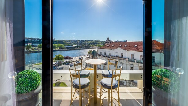 Un balcon avec une table et des chaises, donnant sur une rivière et des bâtiments historiques.