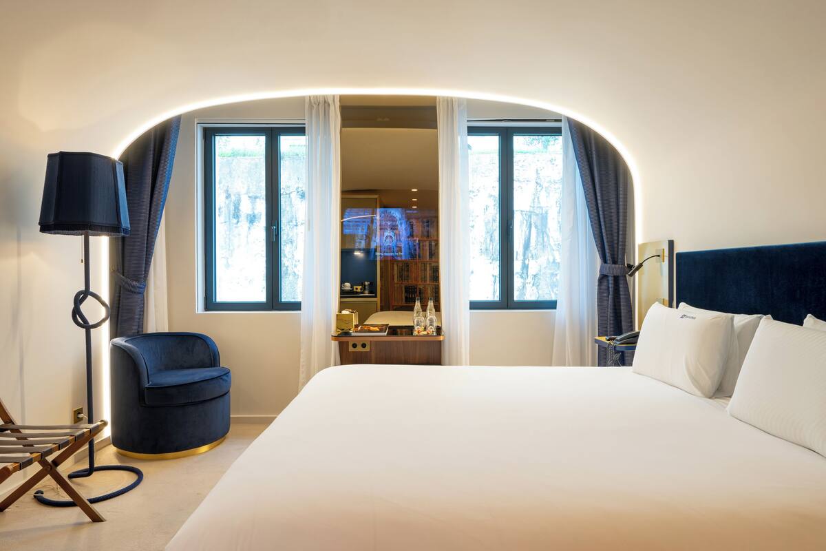 Een hotelkamer met een groot bed, een bureau, een stoel en zicht op het interieur door een deuropening.