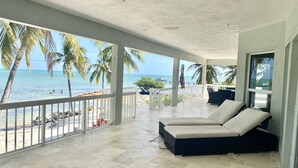 A covered outdoor area with a view of the ocean, featuring a seating area with two white cushioned chairs and a small table. - Keys home overlooking the ocean and beautiful sunrises! (Islamorada)