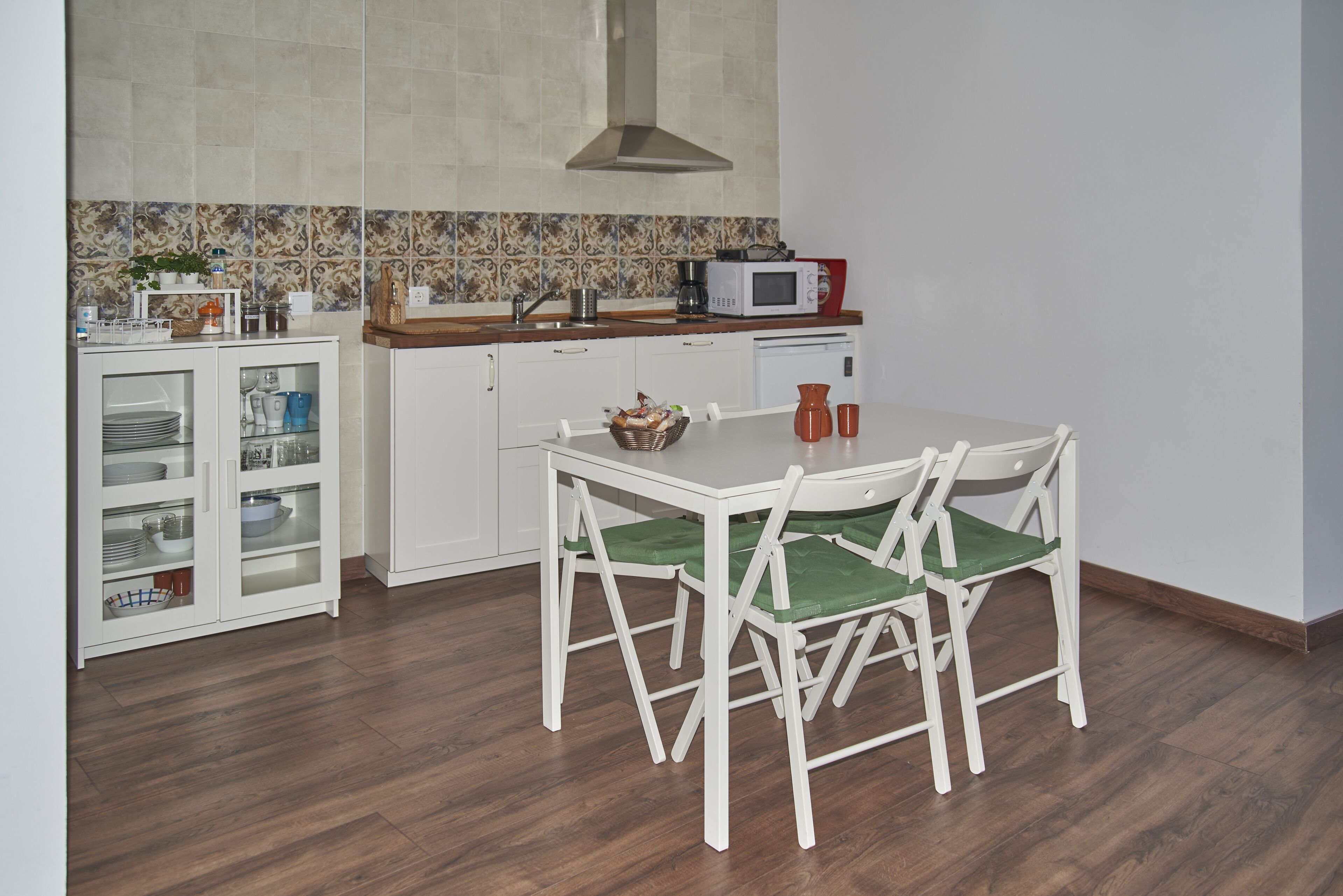 Een compacte keuken met witte kastjes, een magnetron en een eettafel met stoelen.