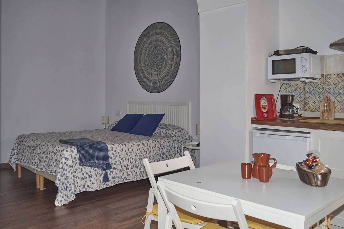 A bedroom with a bed, bedside table, and a small kitchenette area with a microwave and coffee maker.