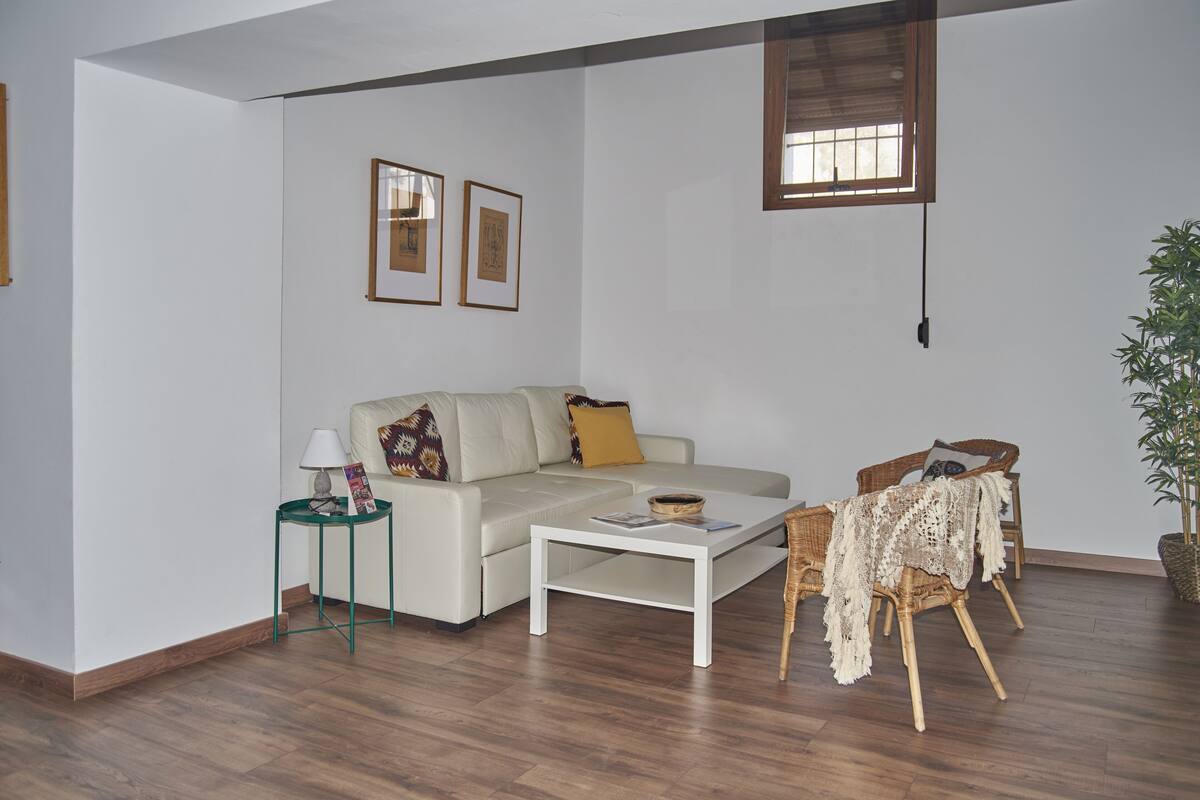 A living room with a sofa, coffee table, side table, wicker chair, and a potted plant.