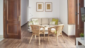 Una stanza con una porta in legno, un divano bianco con cuscini, due poltrone in vimini e un tavolino.