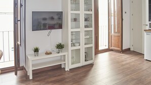 Un soggiorno moderno con una TV a schermo piatto, un mobile bianco con ante in vetro e un pavimento in legno.