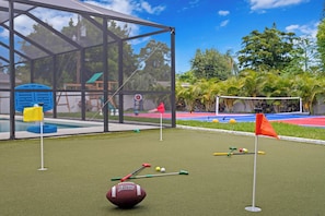 A miniature golf course with a netted enclosure, artificial turf, and golf balls.