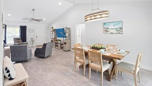 A spacious living area with a dining table, chairs, and a ceiling fan.