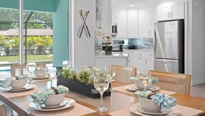 A modern kitchen with white cabinets, a stainless steel refrigerator, and a dining area with a table set for six with wine glasses and plates.