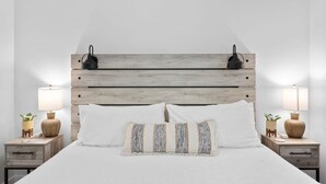 A neatly made bed with white linens, two bedside lamps, and a wooden headboard.