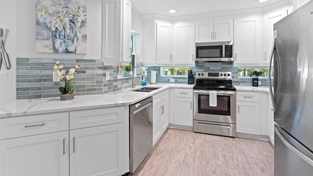 A modern kitchen with white cabinets, stainless steel appliances, and a tiled backsplash.