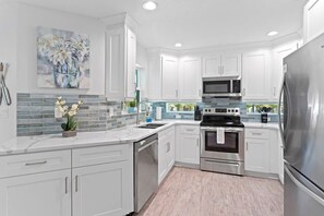 A modern kitchen with white cabinets, stainless steel appliances, and a tiled backsplash. - Pickleball, Axe Throwing, Mini-Golf, Bowling, IMG (Bradenton)