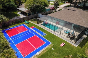 A residential property with a swimming pool, tennis courts, and a covered patio area.