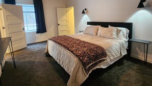 A bedroom with a wooden ceiling, a bed with a patterned blanket, a bedside lamp, and a window with curtains.