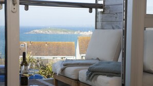 Un balcon avec une table en bois, deux chaises rembourrées et une bouteille de vin.