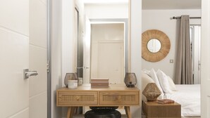 Une chambre d’hôtel avec un bureau en bois, un miroir, un miroir rond fixé au mur, une table de chevet avec une lampe et un lit avec une literie blanche.