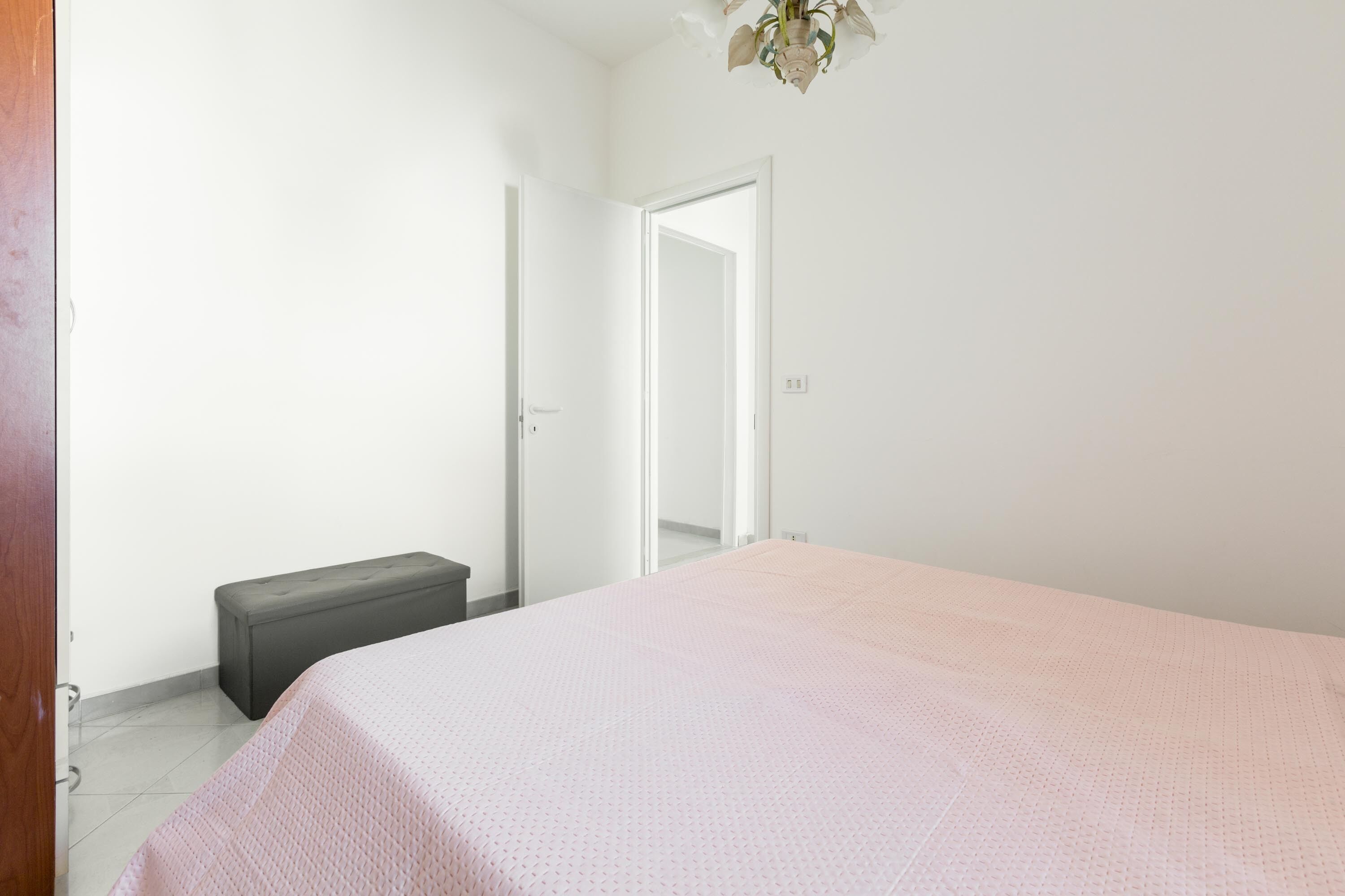 A bedroom with a bed, a bench, and an open door leading to another room.