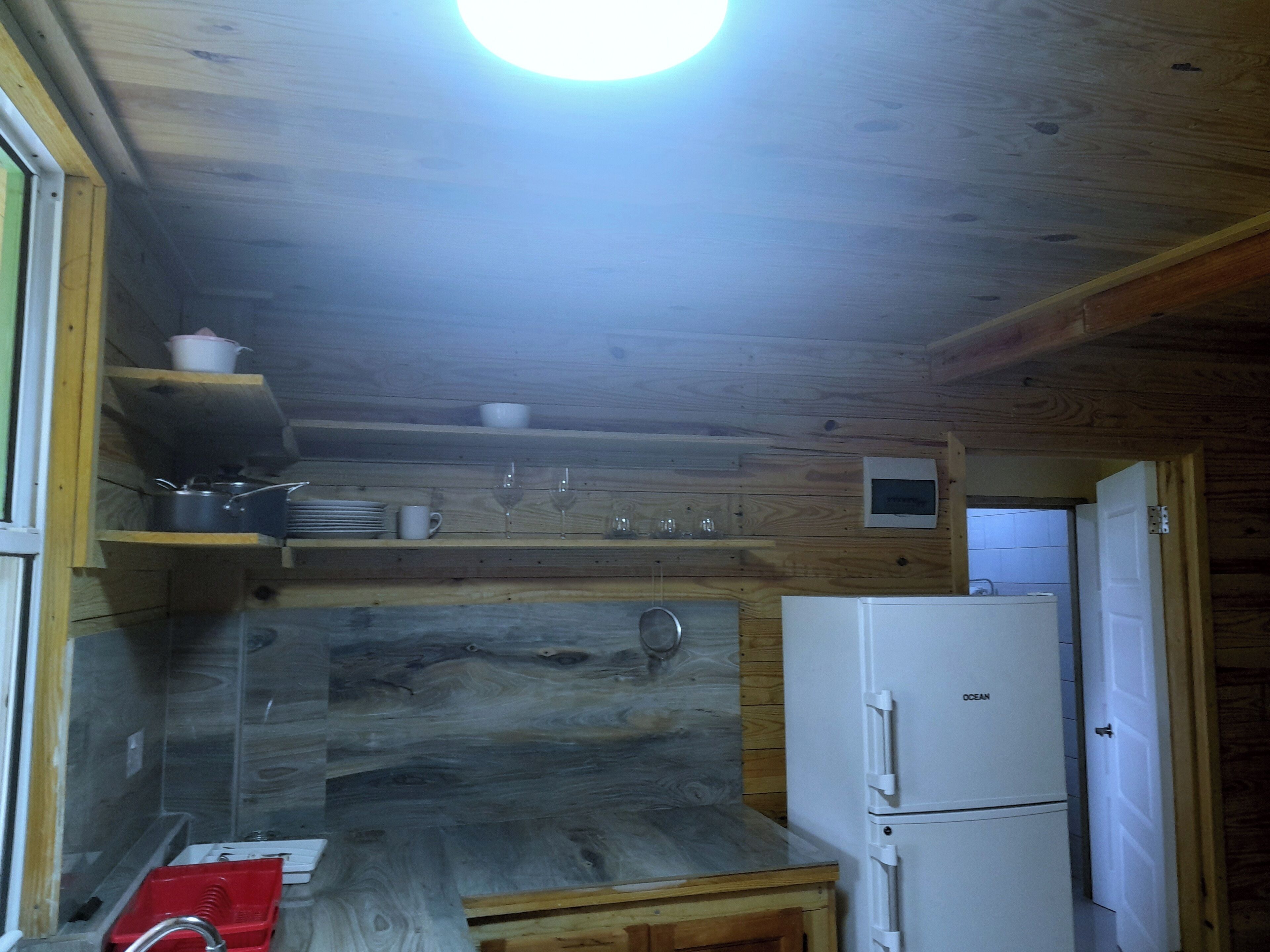 A compact kitchen with wooden walls, a built-in sink, and a white refrigerator.