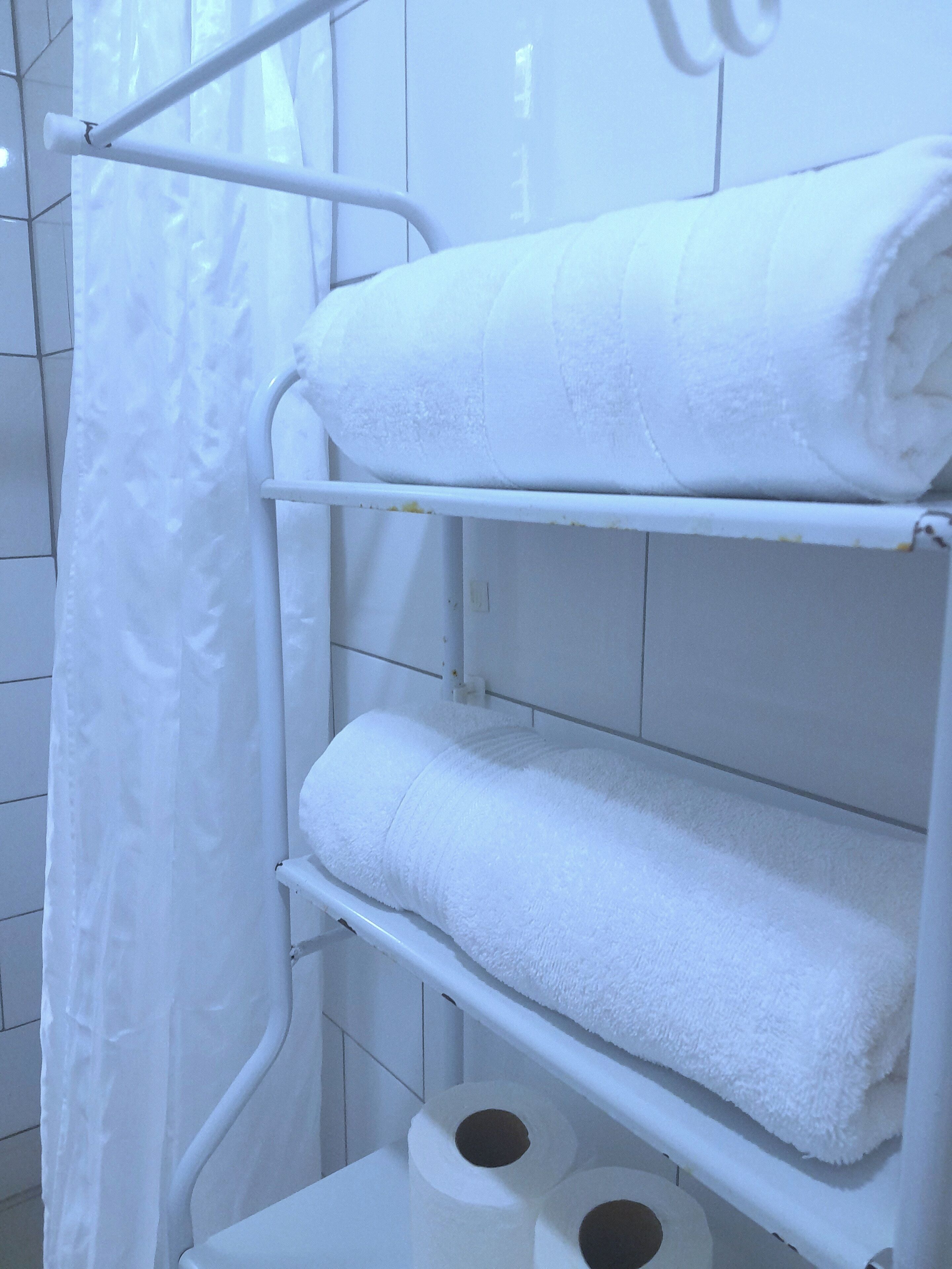 Une salle de bain avec des murs carrelés de blanc, un porte-serviettes blanc avec des serviettes, et deux rouleaux de papier toilette.