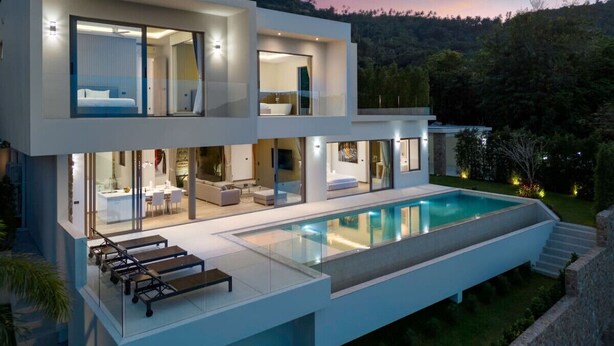 Una casa moderna de dos pisos con piscina, amplias ventanas de vidrio y un interior bien iluminado.