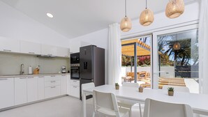 A modern kitchen with white cabinetry, a black refrigerator, and a dining area with white chairs and a table.