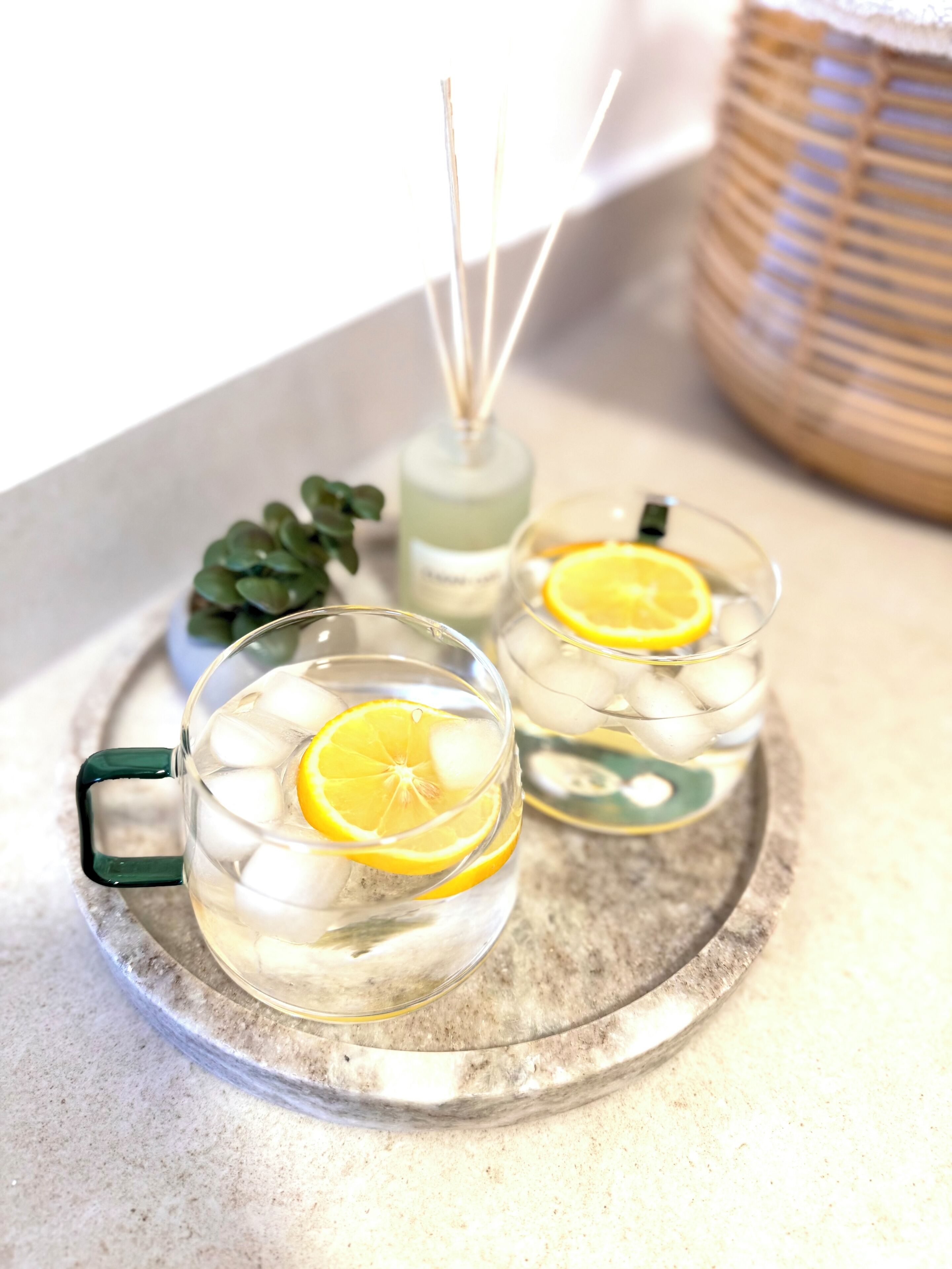 Två genomskinliga glas med isbitar och citronskivor på ett fat.