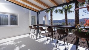A modern outdoor dining area with a wooden ceiling, a long table, and several chairs.