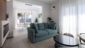 A modern living room with a teal sofa, a round black table, and a dining area in the background.