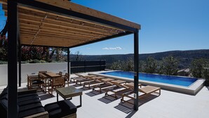 A rooftop pool area with wooden furniture and a pergola.