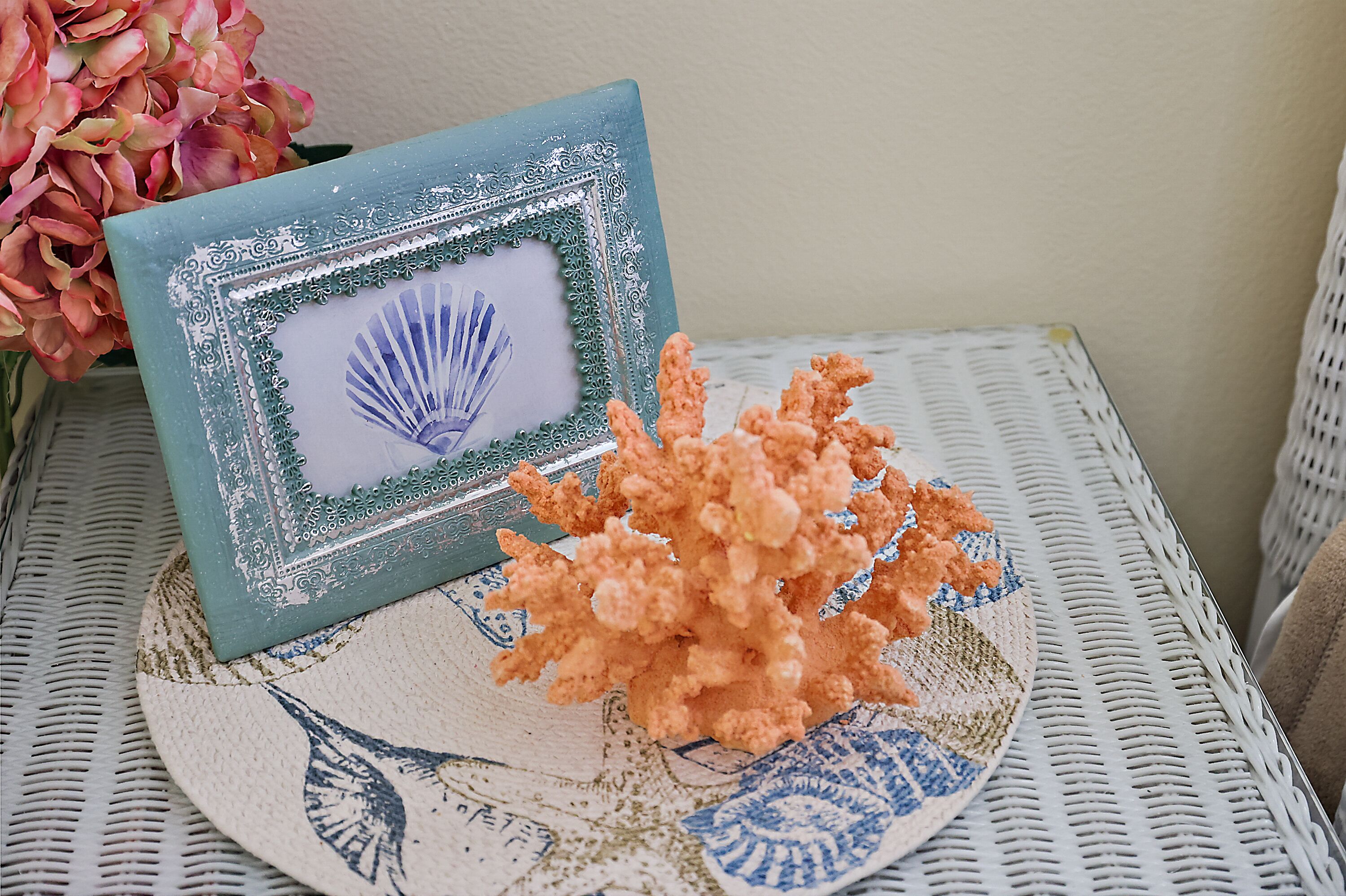 A decorative frame with a seashell design, placed on a woven tablecloth with a blue and white pattern.