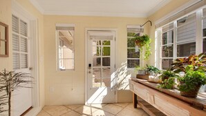 A sunlit hallway with a door leading to a backyard, a bench with potted plants, and a tiled floor. - Home away from home in the heart of charming Winter Park! (Winter Park)