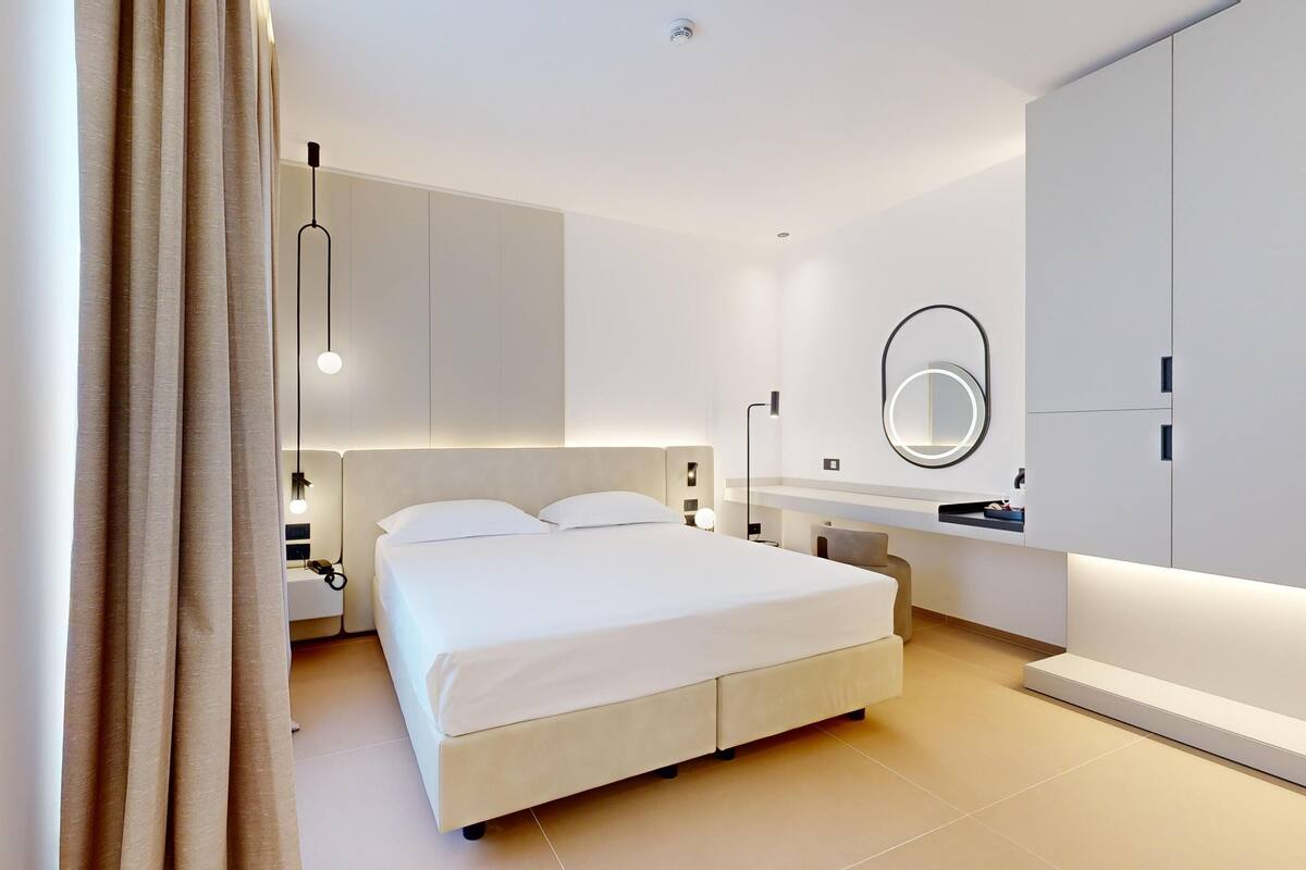 A modern bedroom with a large bed, bedside tables, a mirror, and a wardrobe.