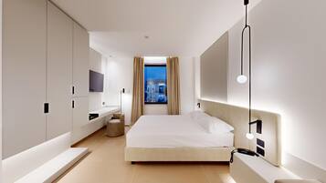 Camera d'albergo moderna con un letto grande, una TV a muro, un comodino e vista sulla città di notte.