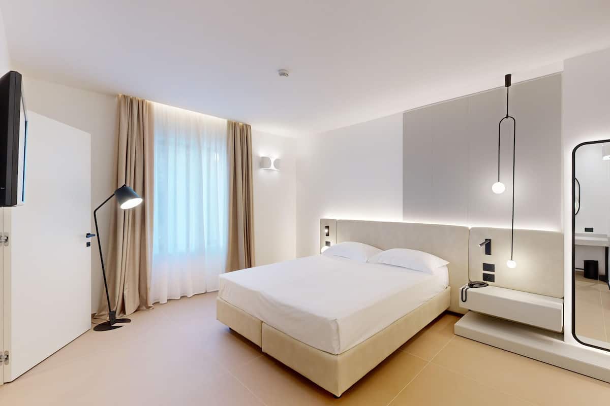 A modern hotel room with a large bed, a bedside table, a mirror, and a flat-screen TV.