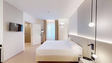 A modern hotel room with a large bed, a flat-screen TV mounted on the wall, and a bathroom visible through an open door.