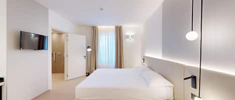 Una habitación de hotel moderna con una cama grande, un televisor de pantalla plana montado en la pared y un baño visible a través de una puerta abierta.
