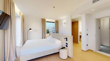A modern hotel room with a bed, a bedside table, a lamp, and a view of the city through the window.