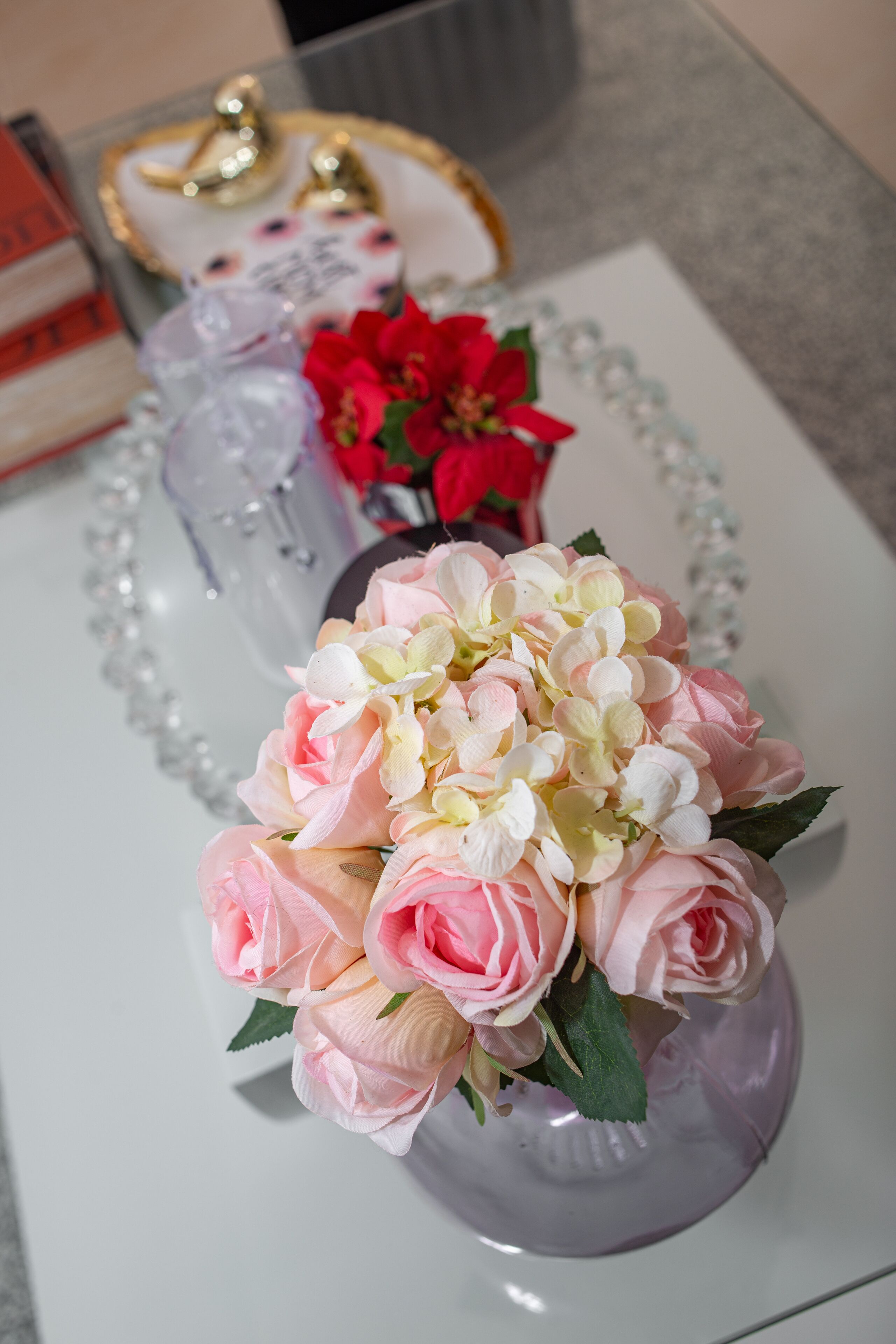 Une table ornée d’un vase contenant des fleurs roses et blanches, d’une bouteille en verre transparent et d’une étoile de Noël rouge.