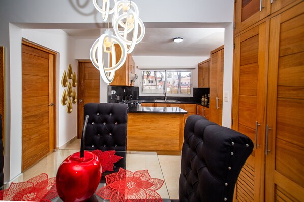 A modern kitchen with wooden cabinets, a black countertop, and a central island. There are two black upholstered chairs with a red decorative item on the table. - Brand new oceanfront condo  in Cabarete (Cabarete)